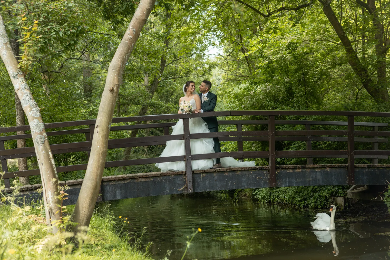 Het bruidspaar op een houten bruggetje in het park, met een zwaan in het water