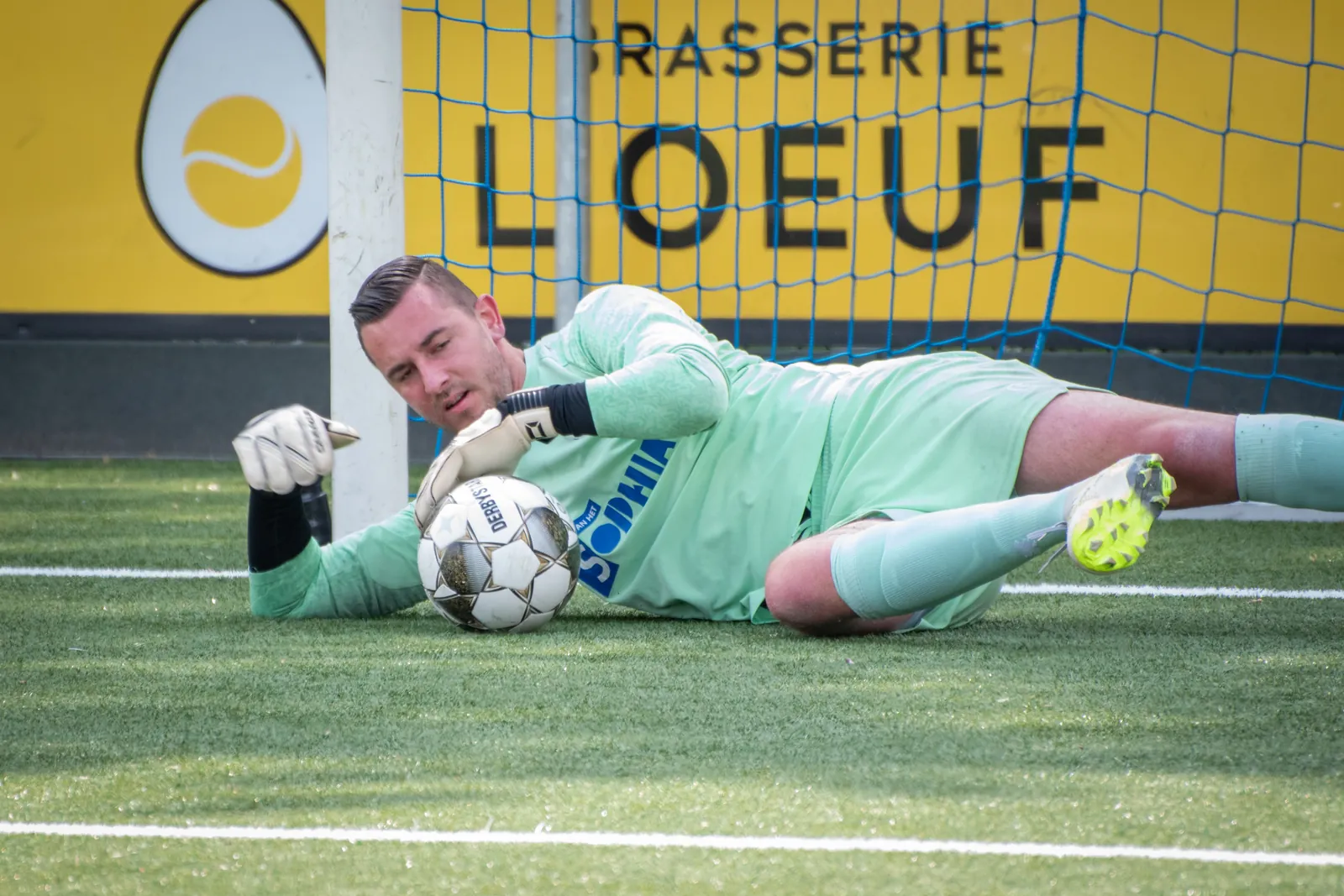 Keeper van CVV Zwervers klemt de bal vast bij de paal tegen DCV