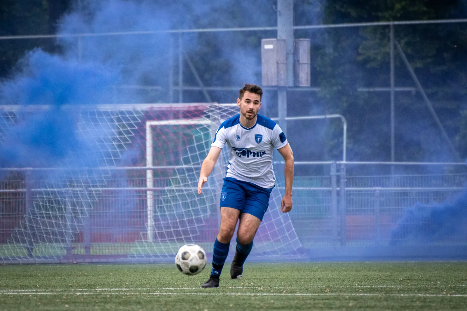 Speler van CVV Zwervers aan de bal in blauwe rook tijdens de kampioenswedstrijd